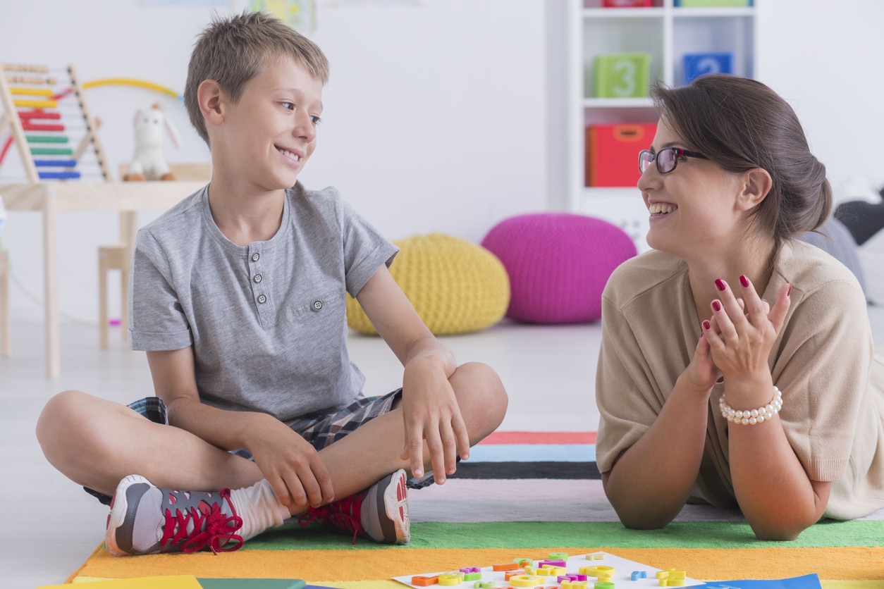 An older child sitting on the ground next to his RBT who is laying down