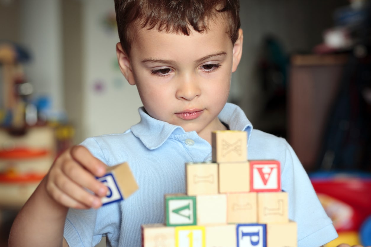 A young boy with autism playing with lettered building blocks