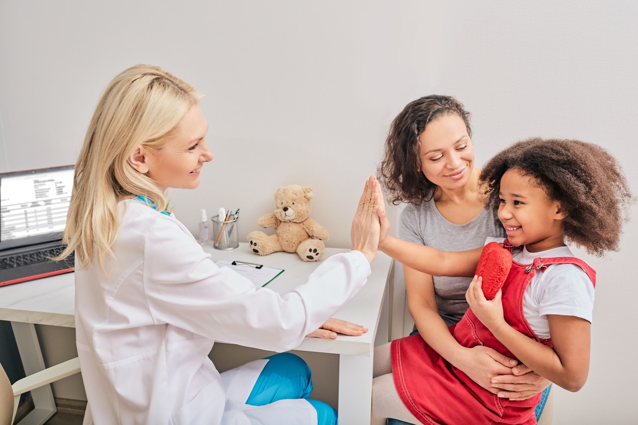 A young girl sitting on her moms lap and high fiving her psychologist