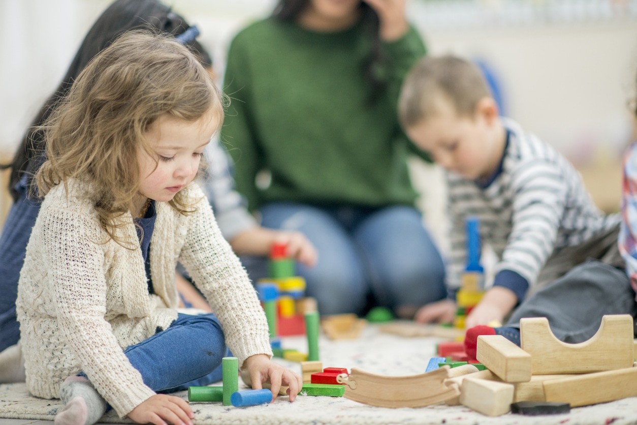 A child with autism playing alone while other children are playing together behind her