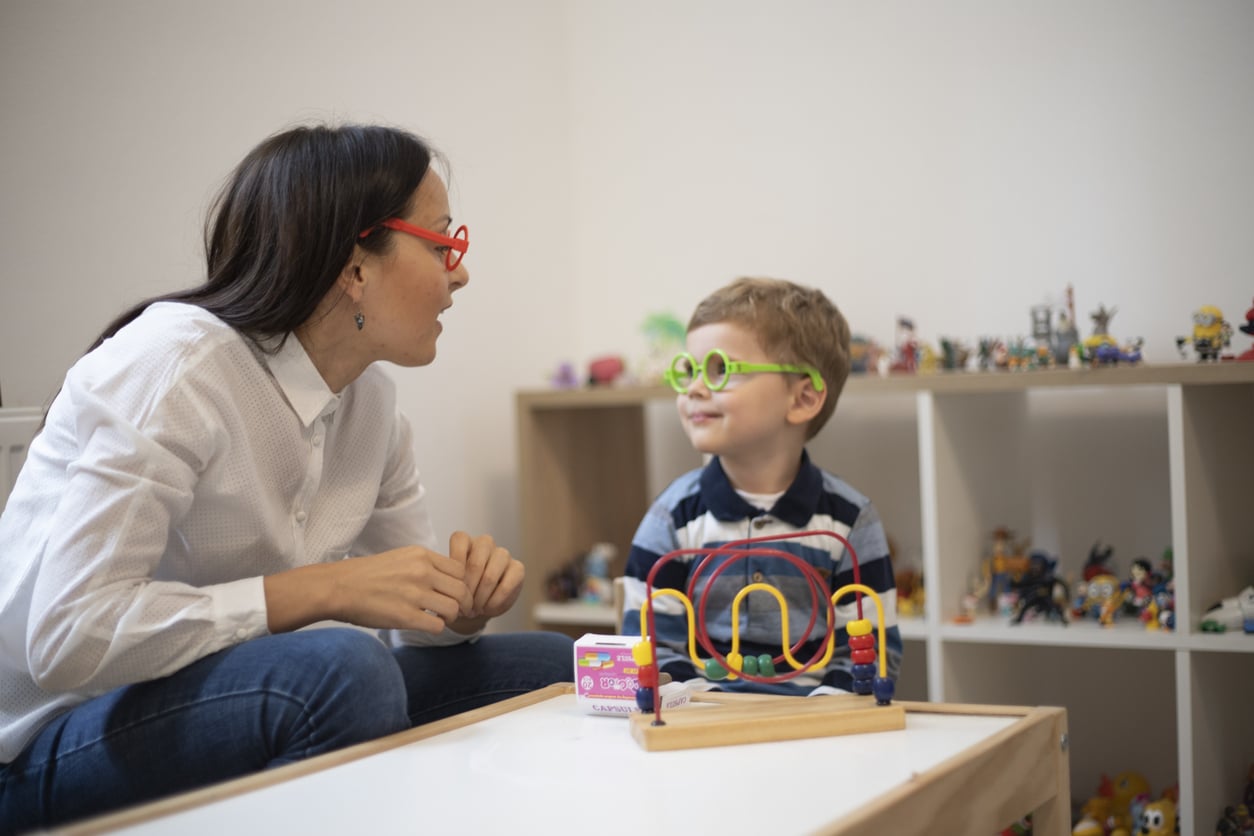 BCBA sitting a table with a young boy with autism and they both are wearing fake colorful glasses