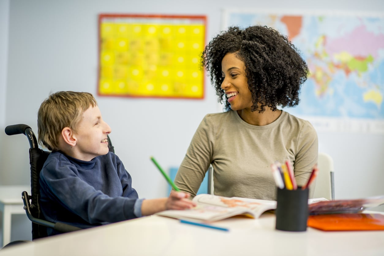 A female RBT sitting at a table with a young boy with cerebral palsy in a wheelchair