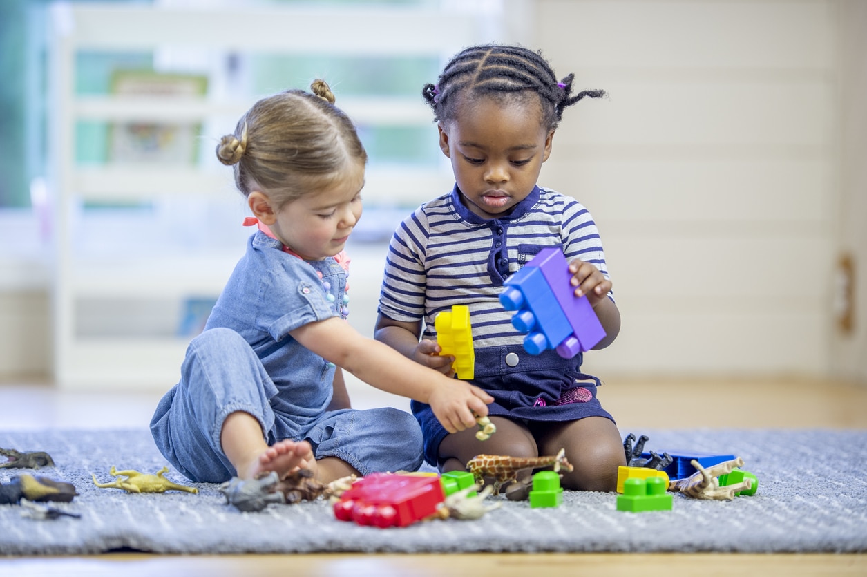 Two preschool-aged children with autism playing with toys together on the floor