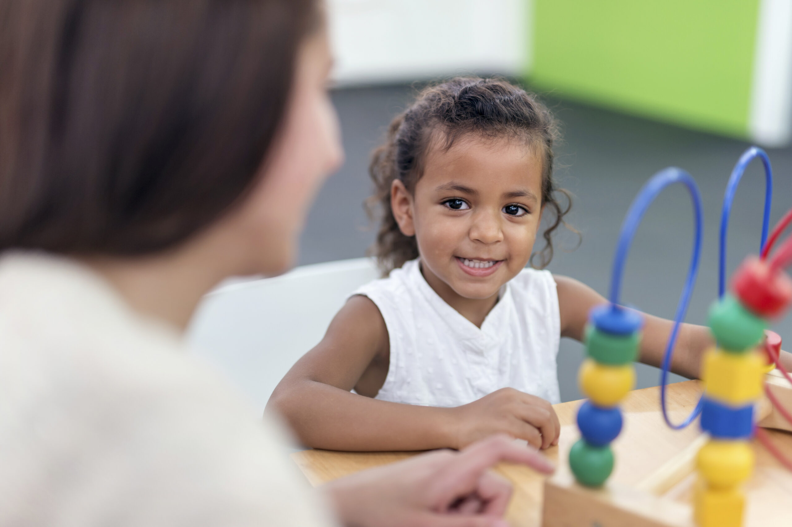 Child smiling while looking and asking questions to her ABA therapist